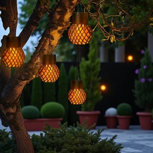 Puede incluir: Faroles decorativos para exteriores con un brillo cálido. Los faroles dorados tienen un diseño de rombos. Cuelgan de una rama de árbol en un jardín, creando un ambiente acogedor. La escena se desarrolla en un jardín.