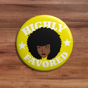 May include: A circular yellow pin-back button featuring a central illustration of a person with a large black afro hairstyle. The text HIGHLY FAVORED is printed in white capital letters around the illustration, flanked by two white stars.
