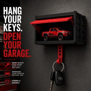 May include: A black wall-mounted key holder shaped like a shipping container with a red door that opens when keys are hung. A red toy pickup truck is displayed inside. The text reads: HANG YOUR KEYS. OPEN YOUR GARAGE. SMART DESIGN DOOR OPENS WHEN KEYS ARE HUNG, SHOWCASE YOUR FAVORITE DIE-CAST CAR, STRONG & DURABLE.