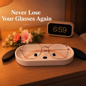May include: A white eyeglasses tray shaped like a dog's face, holding a pair of gold-rimmed glasses. The tray has black accents for the eyes and nose. The text "Never Lose Your Glasses Again" is visible.