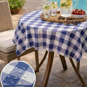 May include: A round outdoor table with a blue and white checkered tablecloth. The table is set with glasses of water, a pitcher of lemonade, and a bowl of strawberries. The tablecloth is water proof.