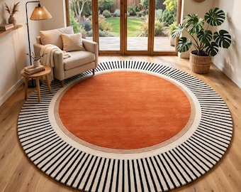 Peut inclure: Un grand tapis circulaire avec un centre orange brûlé uni, une fine bordure beige et un large anneau extérieur composé de rayures radiales noires et blanches alternées. Le tapis est posé sur un parquet en bois clair.