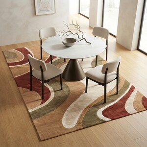 May include: A round white marble dining table with a conical bronze base, surrounded by four chairs with dark wood frames and cream-colored upholstery. A decorative bowl and a branch sit on the table, placed atop a large rug with wavy patterns.