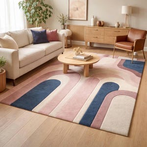 May include: A rectangular area rug featuring a geometric pattern of overlapping arches in shades of dusty pink, cream, and navy blue. The rug has a textured pile and is positioned on a light-colored wooden floor in a living room setting.