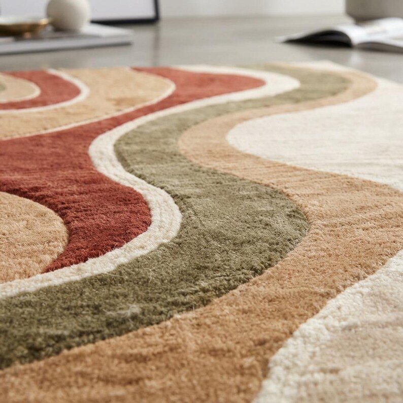 May include: A rectangular area rug featuring a series of wavy, flowing bands in shades of terracotta, olive green, tan, and cream. The surface has a textured, tufted pile construction that creates a soft, layered appearance across the entire rug.