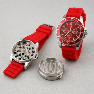 May include: A red wristwatch with a silicone strap and a circular face featuring a red dial with silver hands and markers. Beside it, a disassembled watch-shaped grinder reveals a metallic interior with sharp teeth for grinding herbs.