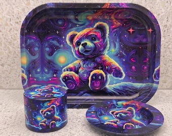 May include: A rectangular metal rolling tray, a cylindrical herb grinder, and a small circular dish, all featuring a vibrant, psychedelic space-themed design with a colorful teddy bear surrounded by swirling nebulae, bright stars, and deep purple hues.