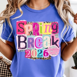 May include: A blue t-shirt with a colorful graphic that says "Spring Break 2026." The text is made up of various fonts and colors, including pink, purple, and green. The graphic is layered on top of a collage of different patterns.