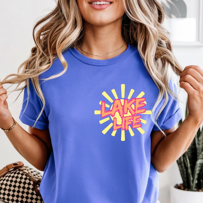 May include: A blue t-shirt with the words "LAKE LIFE" in a yellow and orange design. The text is surrounded by yellow sun rays. The shirt has short sleeves and a crew neck.