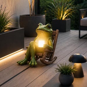 Può includere: Una statua di rana verde su una sedia a dondolo tiene in mano una lanterna luminosa. La scena all'aperto comprende una terrazza in legno, piante in vaso e un tavolino con una lampada a forma di fungo. L'illuminazione crea un'atmosfera calda.