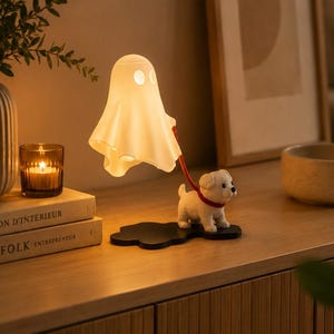 Könnte beinhalten: Eine weiße, geisterförmige Lampe mit zwei Augenausschnitten, die über eine rote Leine mit einer kleinen weißen Welpenfigur verbunden ist. Die Lampe und der Welpe sind auf einem schwarzen, wolkenförmigen Sockel montiert und bilden eine leuchtende Figur.