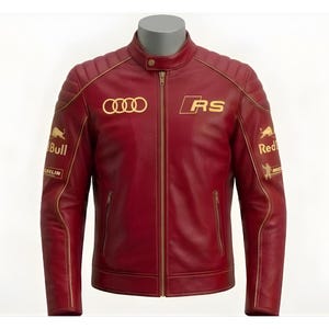 May include: A burgundy leather jacket with gold accents and logos. The jacket features a stand-up collar, a front zipper, and multiple embroidered logos, including "AUDI", "RS", and "Red Bull". The jacket has a quilted design on the shoulders.