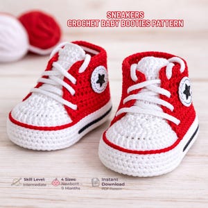 Puede incluir: Un par de patucos de bebé de ganchillo rojos y blancos, que parecen zapatillas deportivas. Los patucos tienen cordones blancos, un emblema de estrella negra en el lateral y una raya negra a lo largo de la suela. El texto "SNEAKERS CROCHET BABY BOOTIES PATTERN" es visible.