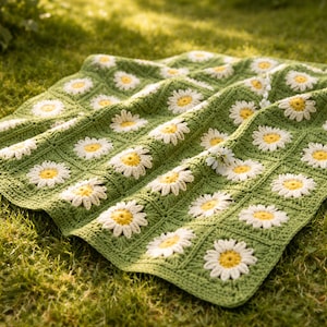 Può includere: Una coperta all'uncinetto fatta a mano con un motivo a margherita. La coperta presenta uno sfondo verde con fiori di margherita bianchi e gialli. Ideale per un letto o un divano.