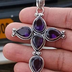 Peut inclure: Un pendentif en forme de croix composé de quatre améthystes violettes taillées en poire et serties dans de l'argent poli. Le design présente de petites perles d'argent entre chaque pierre et une bélière décorative en argent sur le dessus.