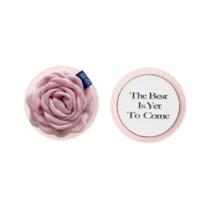 Puede incluir: Dos objetos redondos rosas sobre fondo blanco. Uno presenta una rosa de tela con una etiqueta azul "JUEVES". El otro tiene el texto "The Best Is Yet To Come" en negro sobre un círculo blanco.