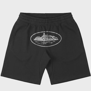 May include: Black shorts with an elastic waistband and a silver oval graphic on the back. The graphic depicts a detailed illustration of a building on an island. The shorts are made of a soft material.
