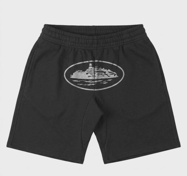 May include: Black shorts with an elastic waistband and a silver oval graphic on the back. The graphic depicts a detailed illustration of a building on an island. The shorts are made of a soft material.