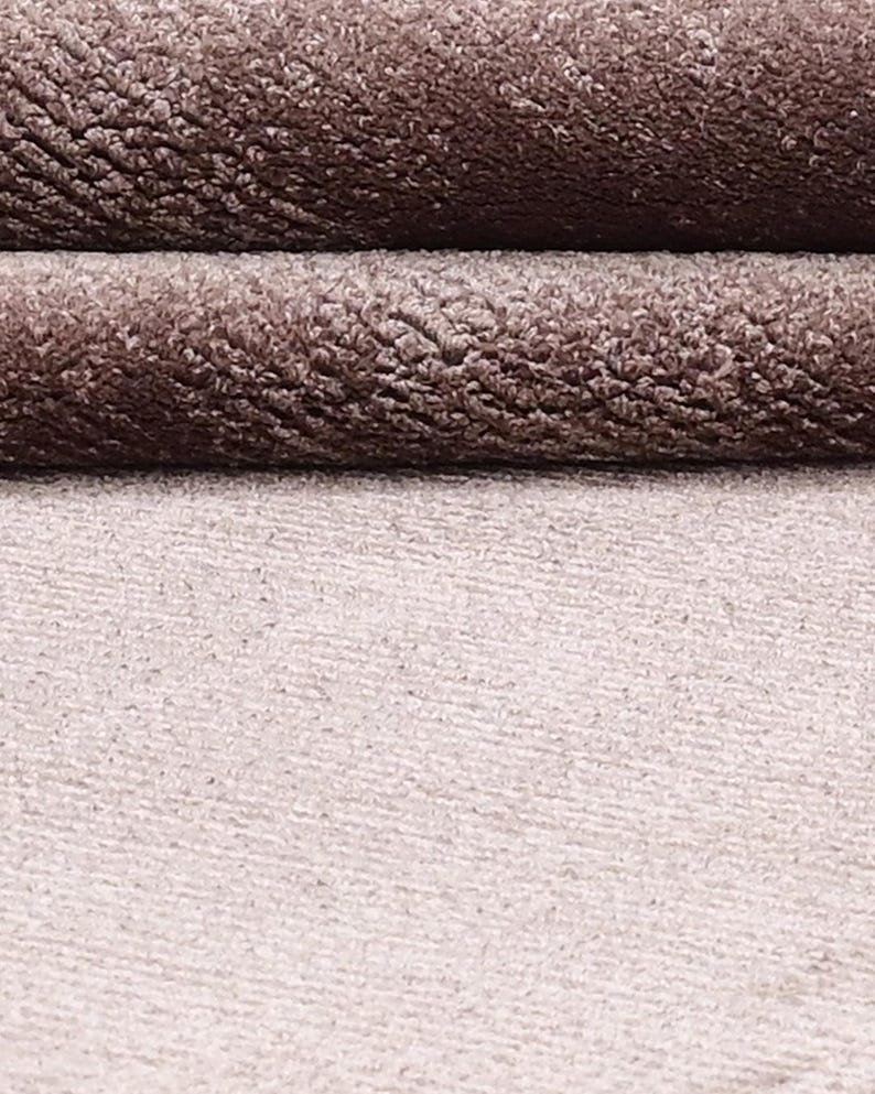 Puede incluir: Primer plano de una tela texturizada en tonos marr&oacute;n y beige. La parte superior presenta dos capas dobladas de un material afelpado y aterciopelado, mientras que la parte inferior muestra una tela m&aacute;s lisa y de color m&aacute;s claro. Las texturas crean un efecto de capas.