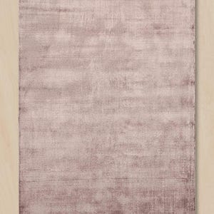 Puede incluir: Una alfombra rectangular de color malva apagado con un aspecto desgastado y texturizado. El color de la alfombra es una mezcla de tonos claros y oscuros de malva, creando un efecto sutil y envejecido. La alfombra probablemente est&aacute; hecha de un material suave.