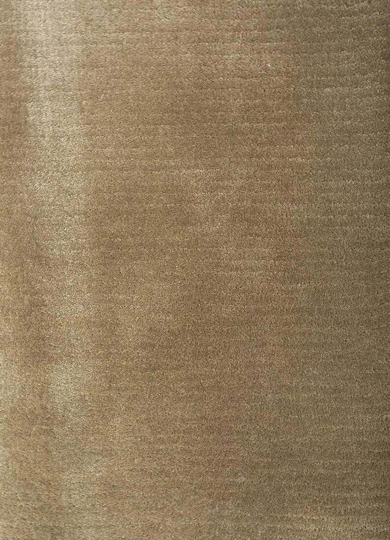 Pu&ograve; includere: Primo piano di un tessuto strutturato marrone dorato. Il materiale ha un aspetto morbido e felpato con sottili variazioni di colore e consistenza, creando un aspetto ricco e invitante. La superficie del tessuto riflette la luce, esaltando la sua profondit&agrave; e il suo calore.