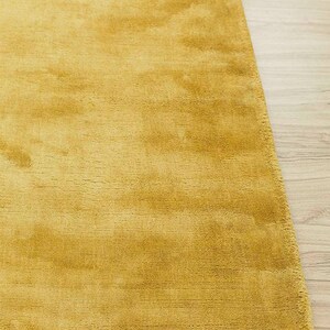 May include: Mustard yellow area rug with a soft, textured surface. The rug is rectangular and has a plush appearance, suitable for a living room or bedroom. The rug's color is a warm, inviting tone.