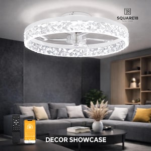 May include: A white ceiling fan with a crystal-studded ring light. The fan is in a modern living room setting with a gray sofa, coffee table, and remote control. The text "DECOR SHOWCASE" is at the bottom.