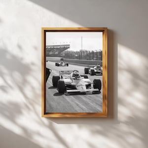 May include: Monochrome framed print depicting Formula 1 cars racing on a track. The leading car, bearing the number 1 and the Marlboro logo, is sharply in focus. The print is encased in a wooden frame, enhancing the vintage feel of the racing scene.