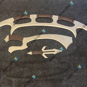 May include: A set of three silver-toned metal blades with brown wrapped handles. The largest is a wide, curved crescent blade with three cutouts, the middle is a curved sickle-style blade, and the smallest is a pointed, double-edged dagger.