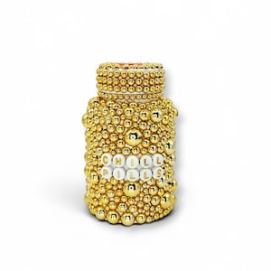 Op de afbeelding: Een decoratieve gouden pillenfles bedekt met kleine, ronde, gouden kralen. De fles heeft een wit etiket met de woorden "CHILL PILLS" in witte letterkralen. De fles staat op een witte achtergrond.