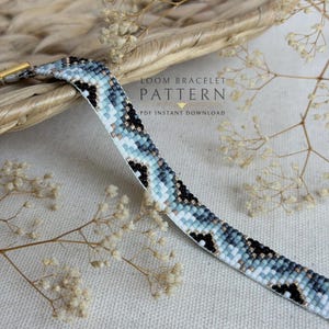 Może przedstawiać: Tkana bransoletka z koralików z geometrycznym wzorem w odcieniach jasnego błękitu, szarości, bieli i czerni. Tekst LOOM BRACELET PATTERN PDF INSTANT DOWNLOAD jest nadrukowany na środku. Bransoletka jest prezentowana z suszonymi kwiatami.