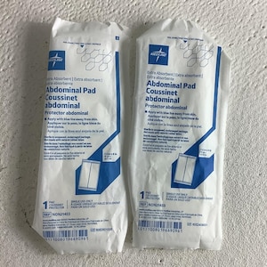 May include: Two white Medline abdominal pads in individual sterile packaging. Each package features blue text and graphics, including the product name, instructions to apply with the blue line away from skin, and dimensions of 7.5 inches by 8 inches.