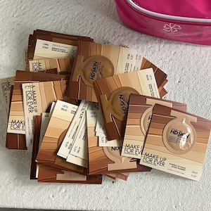 May include: A collection of Make Up For Ever HD Skin foundation sample cards featuring various skin tone shades. Each square card displays the brand name, product name, and a circular blister pack containing liquid foundation.