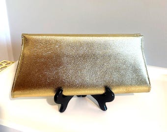May include: A rectangular clutch bag with a metallic gold finish and a textured surface. The bag features a structured, elongated shape with clean, straight edges and a smooth, reflective appearance that catches the light across its surface.