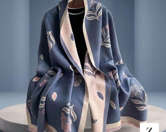 以下が含まれることがあります： 葉と花が繰り返されるフローラルパターンのブルーとライトピンクのショール。前面の縁には幅広でコントラストの効いたライトピンクのボーダーがあり、裾にはフリンジがあしらわれています。黒いベースレイヤーの上に掛けられています。