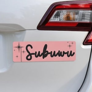Puede incluir: Una pegatina rectangular rosa para parachoques de coche con la palabra "Subuwu" en escritura cursiva negra. La pegatina tiene diseños de estrellas a cada lado del texto. La pegatina está adherida a la parte trasera de un coche blanco.