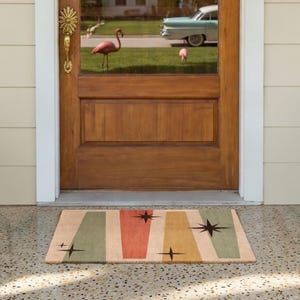 Pode incluir: Um tapete de porta de estilo retro com um design moderno de meados do século. O tapete apresenta listras verticais em verde, laranja e amarelo, com detalhes de estrelas pretas. Colocado em frente a uma porta de madeira.