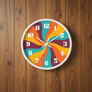 May include: A round wall clock with a white frame. The clock face features a colorful, retro design with swirling bands of teal, orange, yellow, and purple. White numerals mark the hours. The clock is mounted on a wooden wall.