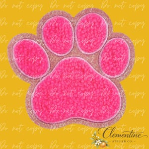 May include: A bright pink paw print patch with a textured, fuzzy surface and a glittery border. The design features four small rounded toe pads above a larger central pad, all outlined in a shimmering material against a solid yellow background.
