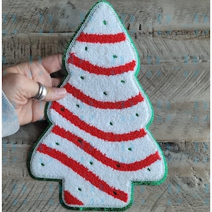 May include: A Christmas tree-shaped patch featuring a white textured surface with diagonal red stripes and small green embroidered dots. The entire shape is outlined with a vibrant green border, creating a distinct festive holiday design.
