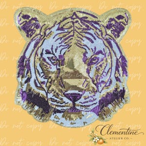 Puede incluir: Un diseño de cabeza de tigre con lentejuelas doradas, moradas y blancas. El diseño muestra la cara del tigre con rayas detalladas, sobre un fondo amarillo. Adecuado para ropa o accesorios.