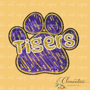 May include: A sequined patch shaped like a paw print in purple and gold. The word Tigers is written across the center in gold sequins with a white outline. The design features a black border and is set against a light orange background.