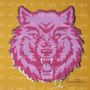 May include: A patch featuring a stylized wolf head design in shades of pink and light purple. The wolf is depicted with an open mouth showing teeth, rendered in a textured, embroidered style with a silver-toned border against a yellow background.