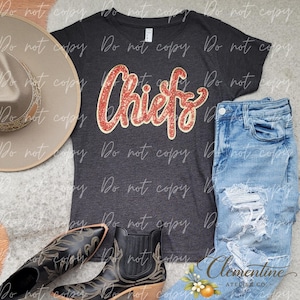 Könnte beinhalten: Ein dunkelgraues Kurzarm-T-Shirt mit dem Wort Chiefs in roter Glitzerschrift, ein beigefarbener Hut mit breiter Krempe, eine hellblaue Jeans mit Used-Look sowie schwarze Lederstiefeletten mit dekorativem Stickmuster an den Seiten und Zehen.
