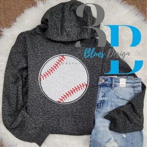 May include: A gray leopard print hoodie with a baseball graphic. The baseball is white with red stitching and a black outline. The hoodie is paired with blue denim jeans. The text "Blues Design" is visible.
