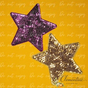 May include: Two five-pointed star-shaped patches featuring dense, reflective sequin embellishments. One star is a vibrant purple color, while the other star is a metallic gold color. Both star patches are positioned against a solid yellow background.