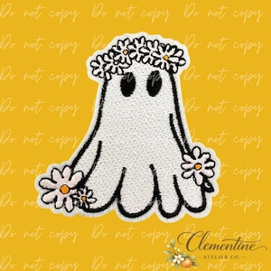 Puede incluir: Un parche bordado que muestra un fantasma blanco con ojos ovalados negros, que lleva una corona de margaritas blancas con centros amarillos. Margaritas blancas adicionales con centros amarillos se sitúan en la base del fantasma a los lados.
