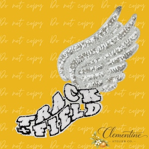 Peut inclure: Un écusson en forme d'aile recouvert de paillettes argentées, placé au-dessus de lettres blanches aux contours noirs formant les mots TRACK FIELD. Le motif présente une surface scintillante et texturée ainsi qu'une typographie en gras.