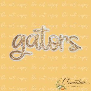 May include: A gold sequin patch featuring the word gators in a cursive script font. The letters are densely covered in small, reflective gold sequins with a white border outline, set against a solid yellow background with a watermark pattern.