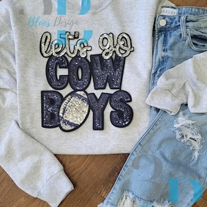 Peut inclure: Un sweat-shirt gris clair avec le texte "Let's Go Cowboys" en paillettes bleu marine et un motif de ballon de football. Le sweat-shirt est associé à un jean bleu clair déchiré. Il s'agit d'un vêtement sur le thème du sport.